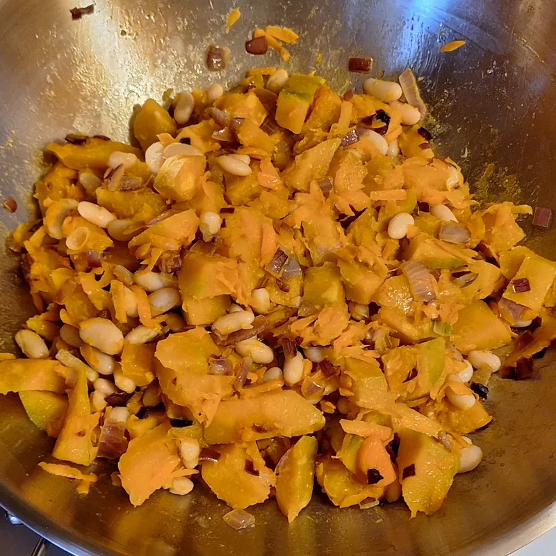 Pumpkin and beans added to the onion and carrot sauté in the pan.