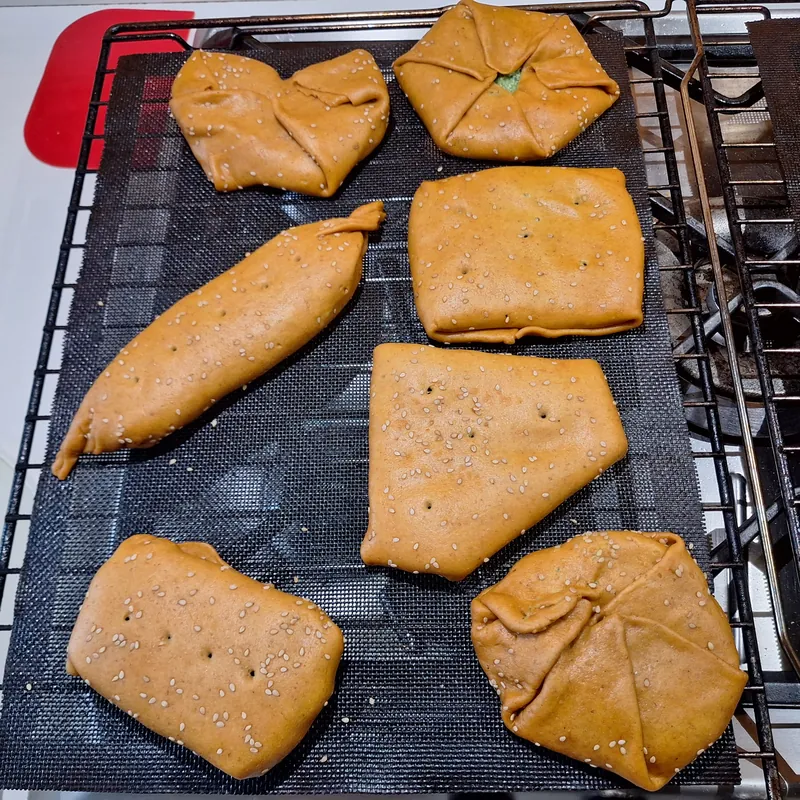 The sealed parmesan parcels, decorated with white sesame seeds, ready to bake