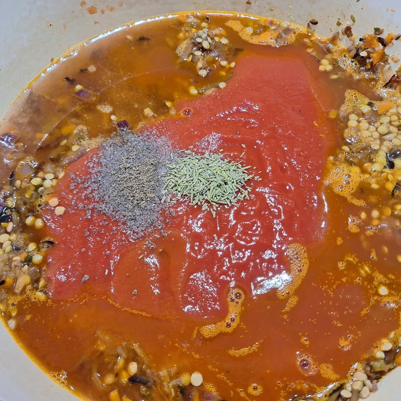 Aggiunti la passata di pomodoro, l'acqua e gli aromi (alloro, pepe), prima di portare a sobbollire e coprire.